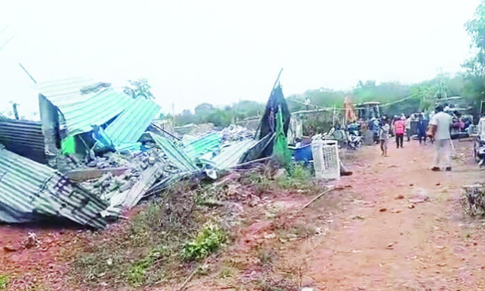 Police and officials carrying out demolition of huts while displaced families stand with belongings