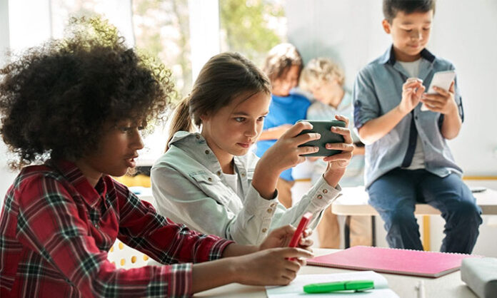 A young child using a laptop while sitting among books, symbolizing the impact of technology and academic pressure on modern childhood.