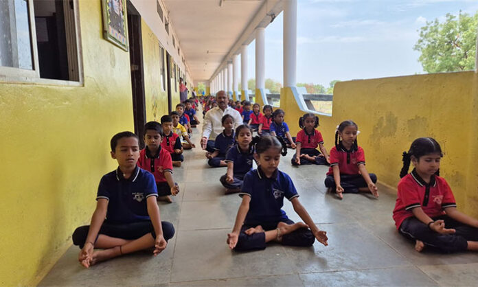 BNR School Chairman Hanumanth Reddy performs yoga with students during the International Yoga Day celebration in Kishtapur Division.