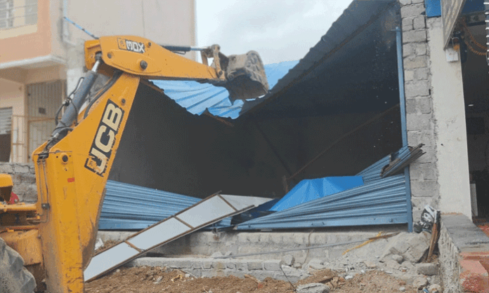 Revenue Department officials demolishing illegal commercial shutters constructed on government land in Jawahar Nagar under the supervision of Revenue Inspector Satyanarayana.