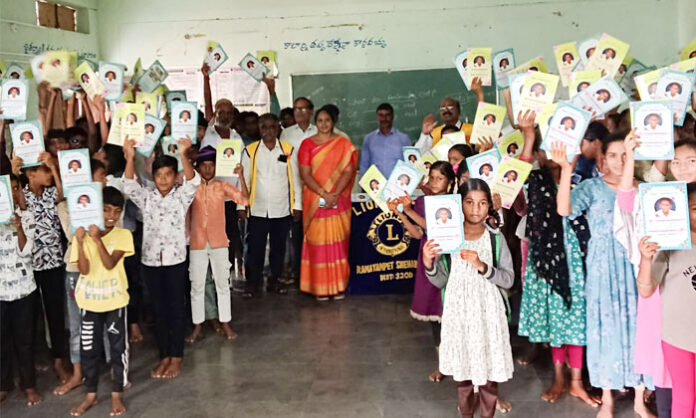 Lions Club members distribute free notebooks to students at Nandivada High School in Tadwai Mandal.