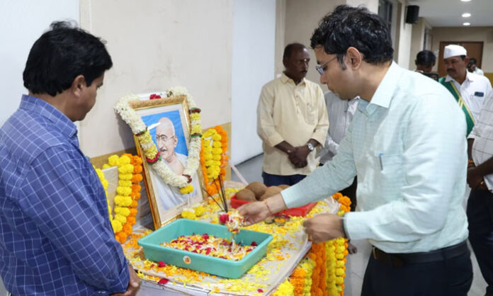 District Collector Bhavesh Mishra garlands a portrait of Mahatma Gandhi during Gandhi Jayanti celebrations at the Collectorate conference hall.