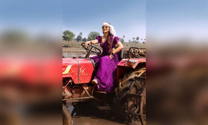 Keerthy Suresh as Latha Reddy in a rustic traditional look for January 12 Vidudala, featuring a purple outfit, headscarf and sunglasses while sitting on a tractor.